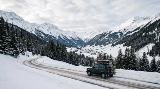 Voiture chargée de skis et de bagages sur une route de montagne enneigée menant vers une station alpine, illustrant le covoiturage vers La Clusaz