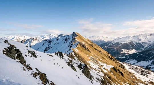 Vue panoramique d'un domaine skiable alpin partagé entre un versant ensoleillé peu enneigé et un versant ombragé recouvert de neige fraîche