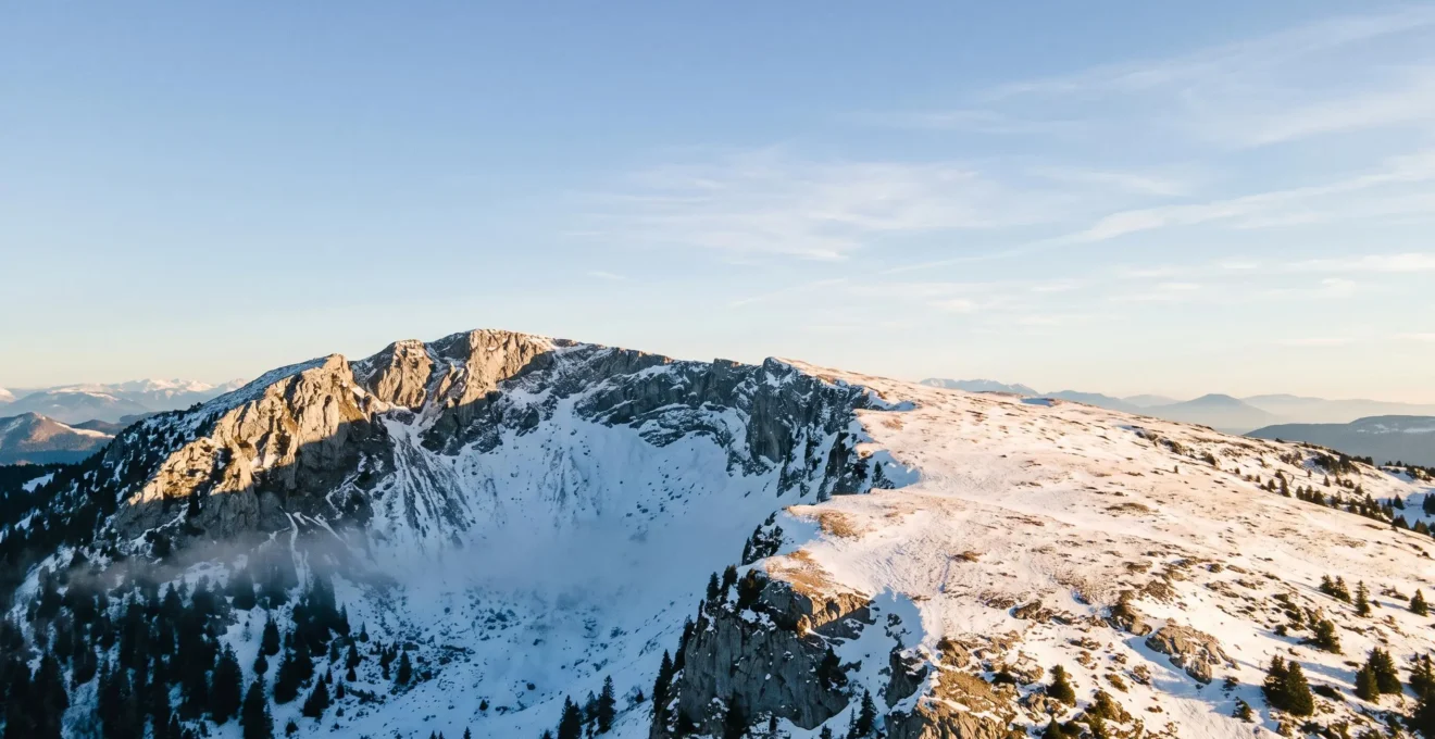 Vue aérienne du massif des Aravis montrant un contraste entre une combe ombragée couverte de neige froide et un versant ensoleillé à la neige transformée, illustrant les micro-climats du massif
