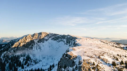 Vue aérienne du massif des Aravis montrant un contraste entre une combe ombragée couverte de neige froide et un versant ensoleillé à la neige transformée, illustrant les micro-climats du massif