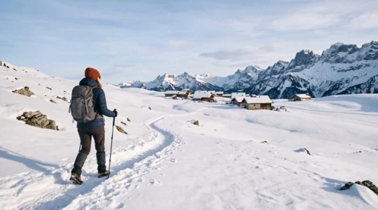 Randonneur avançant seul sur un sentier piéton enneigé face aux sommets des Aravis à l'aube