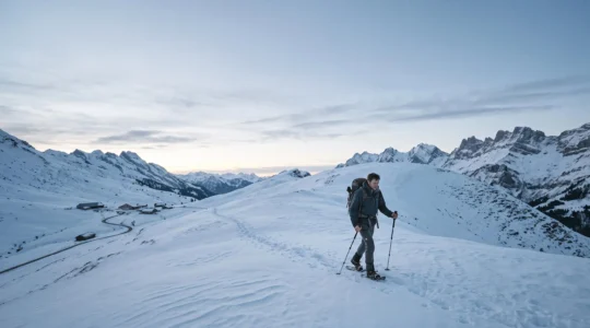 Randonneur en raquettes à neige progressant seul sur une crête enneigée des Aravis au lever du jour, symbolisant le passage de la balade facile à l'itinérance autonome