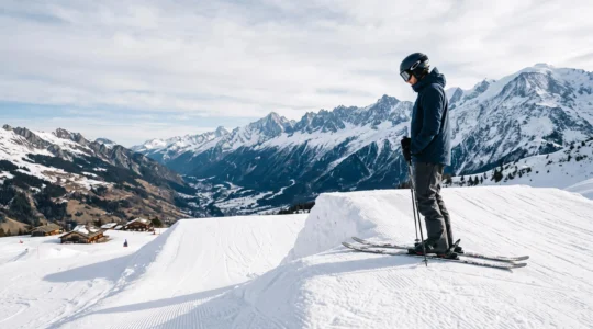 Skieur hésitant au sommet d'un module de snowpark en montagne, dominant les pistes enneigées des Alpes françaises